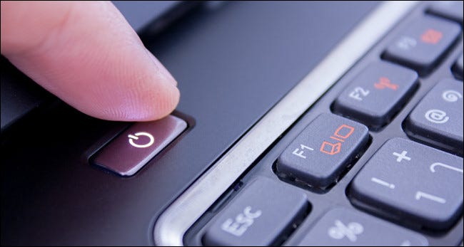 Un dedo presionando el botón de encendido de una computadora portátil.